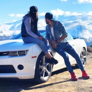 A young couple enjoys a scenic mountainous view while seated on a sports car.